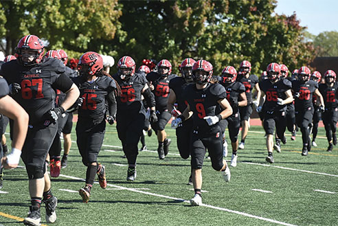 Student football players running on the field. Links to Donor-Advised Funds